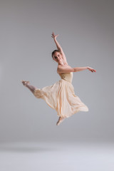 Fototapeta premium Enjoy moving your body with ease! Young cheerful attractive ballerina in jump showing split isolated on grey background.