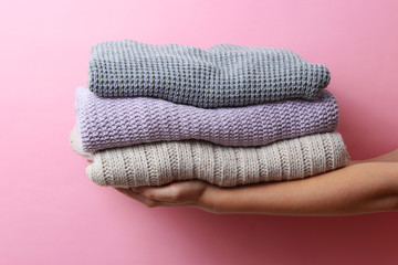 sweaters stacked in a pile in female hands on a colored background. Minimalism