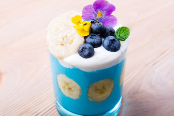 Smoothie dessert with fruits, berries, nuts and flowers on wooden background. Tropical healthy smoothie. Healthy breakfast, vegetarian food, lunch concept