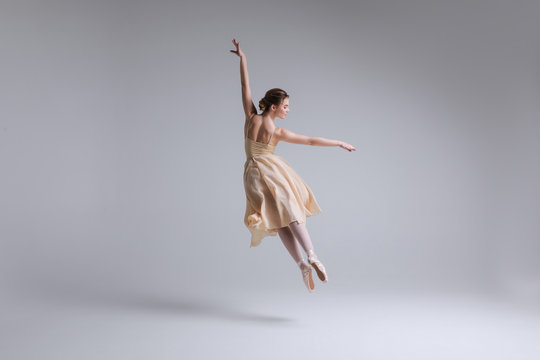 Express yourself! Beautiful tender female ballet dancer with flowing beige fabric dress dancing with grace in the isolated studio.