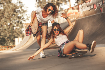 Two female friends playing with skateboard at the skate park.One girl pushing other from...