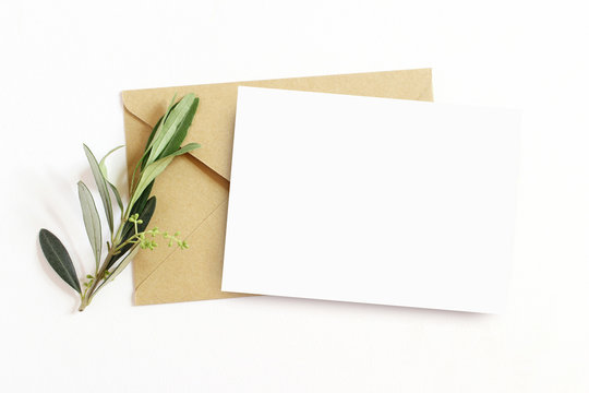 Feminine stationery, desktop mock-up scene. Blank greeting card and craft envelope with olive branch.White table background. Flat lay, top view.