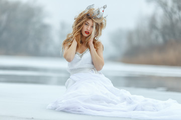 The Snow Queen. Young beautiful girl, blonde, in the image of a snow queen, on ice of a frozen river