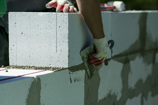 The process of bricklaying. Mason hands installing aerated concrete wall using special glue and tools necessary for brick works. Fresh mortar on aerocrete blocks. Brickwall layer with cement or glue.
