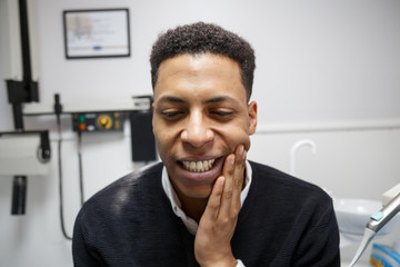 African-American man suffering from toothache and complaining during visit to professional dentist. 