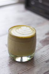 Trendy multicolored lattes. Top view of hot green tea milk or avocado or matcha tea taste with latte art in a cup on wood table. Beautiful foam, glass cups, stylish toning, space for text.