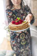 Photo of happy young woman standing at the kitchen in home cooking. Focus on pancakes