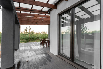 Side view of an open veranda in front of a modern forest cottage. Pine young forest under the...