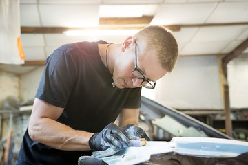 ute guy with glasses pulls the wing from the car with the help of sandpaper on the rough in the garage