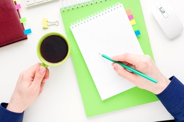 white desktop, men's hands, guy holding Cup of coffee and writes in a notebook, white background with copy space, for advertisement, top view