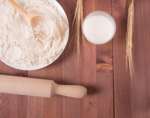 Culinary background - flour, eggs and a wooden rolling pin on a wooden background. Top view