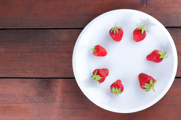 Strawberries on a white plate top view, red berries on a wooden background, fresh strawberries on dark wooden boards, vegetarian food