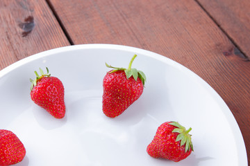 Strawberries on a white plate top view, red berries on a wooden background, fresh strawberries on dark wooden boards, vegetarian food