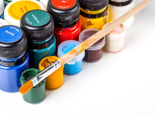 Gouache in jars and brush lying on open jars on white background