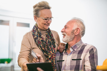 Senior couple using digital tablet in the kitchen at home for online shopping