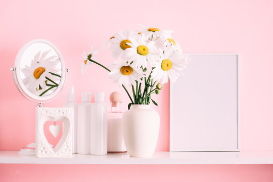 Front view blank mock up of photo frame. Soft pink light bathroom decor for advertising, design, cover, set of cosmetic bottles. Flowers in a vase on a pink wall background, mirror on a wooden shelf 