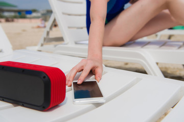 Female hand with phone and speaker at beach