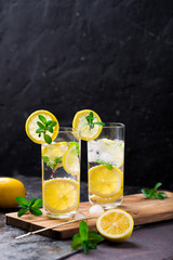 Lemon fruit lime slices caipirinha from Brazil, lemonade mint ice cubes in cold glasses on dark background, alcoholic mojito cockail ice tea green mint leaves, brown sugar spoon, copy space