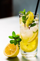 Lemon fruit lime slices caipirinha from Brazil, lemonade mint ice cubes in cold glasses on dark background, alcoholic mojito cockail ice tea green mint leaves, brown sugar spoon, copy space