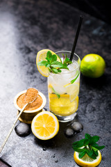 Lemon fruit lime slices caipirinha from Brazil, lemonade mint ice cubes in cold glasses on dark background, alcoholic mojito cockail ice tea green mint leaves, brown sugar spoon, copy space