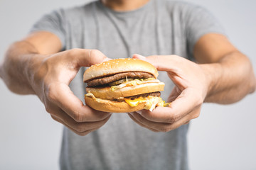 Young man holding a piece of hamburger. Close-Up. Student eats fast food. Burger is not helpful food. Very hungry guy. Diet concept.