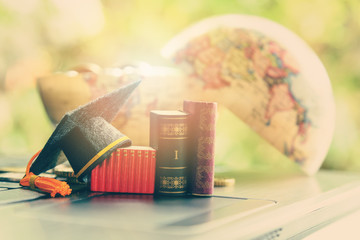 Graduate study abroad program for opening or expand world view concept : Graduation cap or hat, world globe, foreign text book on laptop, depicts achievement or success in online learning / education