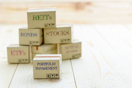 Portfolio and wealth management with risk diversification concept : Small paper cartons / boxes of financial instruments i.e ETFs, REITs, stocks, bonds, mutual funds and commodities, on a wood table.