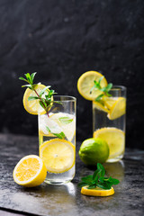 Lemon fruit lime slices caipirinha from Brazil, lemonade mint ice cubes in cold glasses on dark background, alcoholic mojito cockail ice tea green mint leaves, brown sugar spoon, copy space