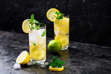 Lemon fruit lime slices caipirinha from Brazil, lemonade mint ice cubes in cold glasses on dark background, alcoholic mojito cockail ice tea green mint leaves, brown sugar spoon, copy space