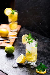 Lemon fruit lime slices caipirinha from Brazil, lemonade mint ice cubes in cold glasses on dark background, alcoholic mojito cockail ice tea green mint leaves, brown sugar spoon, copy space