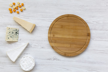 Set of various cheese with round bamboo board on a white wooden background. Copy space. From above,...