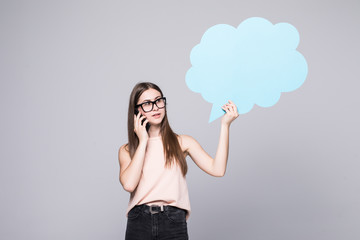 Portrait of a happy woman holding blank speech bubble and talking on mobile phone isolated over gray background