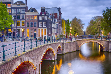 Naklejka premium Nighview of Amterdam Cityscape with Its Canals. Illuminated Bridge and Traditional Dutch Houses At Twilight on The Background.