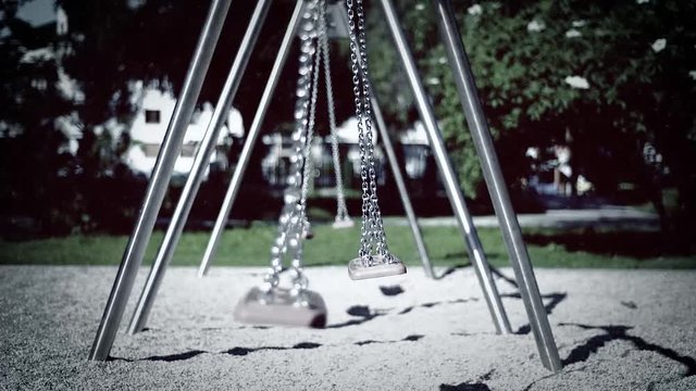 Abandoned empty swings swaying in the wind at children playground outdoors