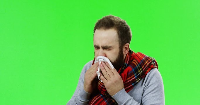Close up of the young ill caucasian man in the warm scarf caughing hard as he having a cold or influenza. Green screen. Chroma key.