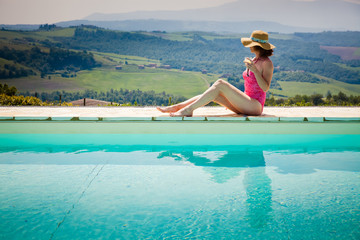 woman sitting by the pool with a cocktail  admiring green ladscape in Tuscany, Italy