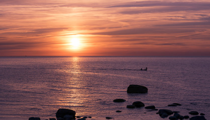 Fishing boat and fishermen on water at a sunset. Tranquil sea with no waves