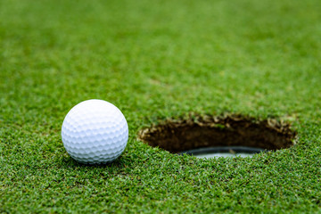 Close up side view of a golf ball on a putting green next to the hole
