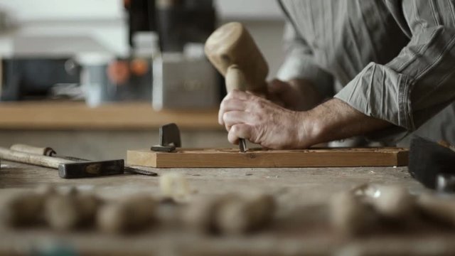 Skilled carpenter carving wood with mallet and chisel
