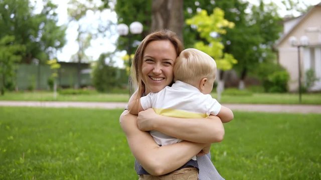 Little blond boy running to his mother. Mom opened her hands and smiling catches the baby. Happy mother, loving son. Picnic outdoors. Green park. Slow motion