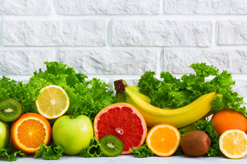 Healthy food fruits grapefruit, lemon, kiwi, apple, banana, orange, green salad background on white painted brick wall. Concept healthy eating diet plan detox sports nutrition.