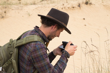 Young male traveler in desert, hipster photographer in hat make photo 