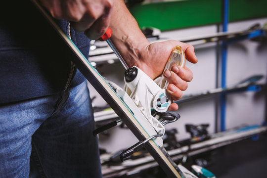 Theme tincture and repair ski equipment ski. Close-up of a Caucasian man's hand use a hand-held screwdriver tool to tweak, twist bindings for ski boots in the workshop