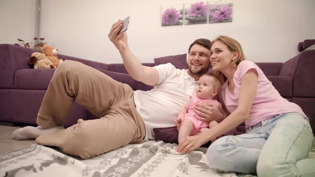 Happy family making selfie at home. Young family with little baby take a picture on mobile phone. Happy togetherness life concept. Father take photo with wife and daughter. Enjoy life