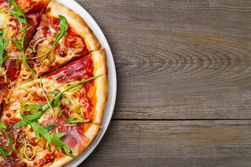 Italian traditional cuisine, pizza, food background. Fresh baked pizza with prosciutto and arugula on wooden table, copy space. Restaurant menu photo, pizzeria, food recipe, pizza delivery concept 
