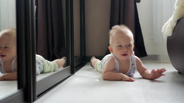 Baby boy play with own reflection in mirror.
