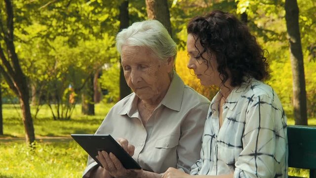 An elderly woman with a daughter with a tablet. Look at the pictures on the tablet.