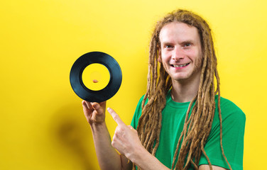 Happy young man holding a vinyl record on a yellow background