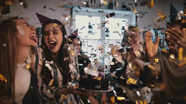 Beautiful European girl holds birthday cake, celebrates with happy multiethnic friends and amazing confetti slow motion.