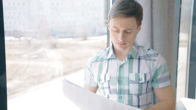 Portrait of businassman reading paper report near the window. Concept of: business people, city view, office interior, paper report.